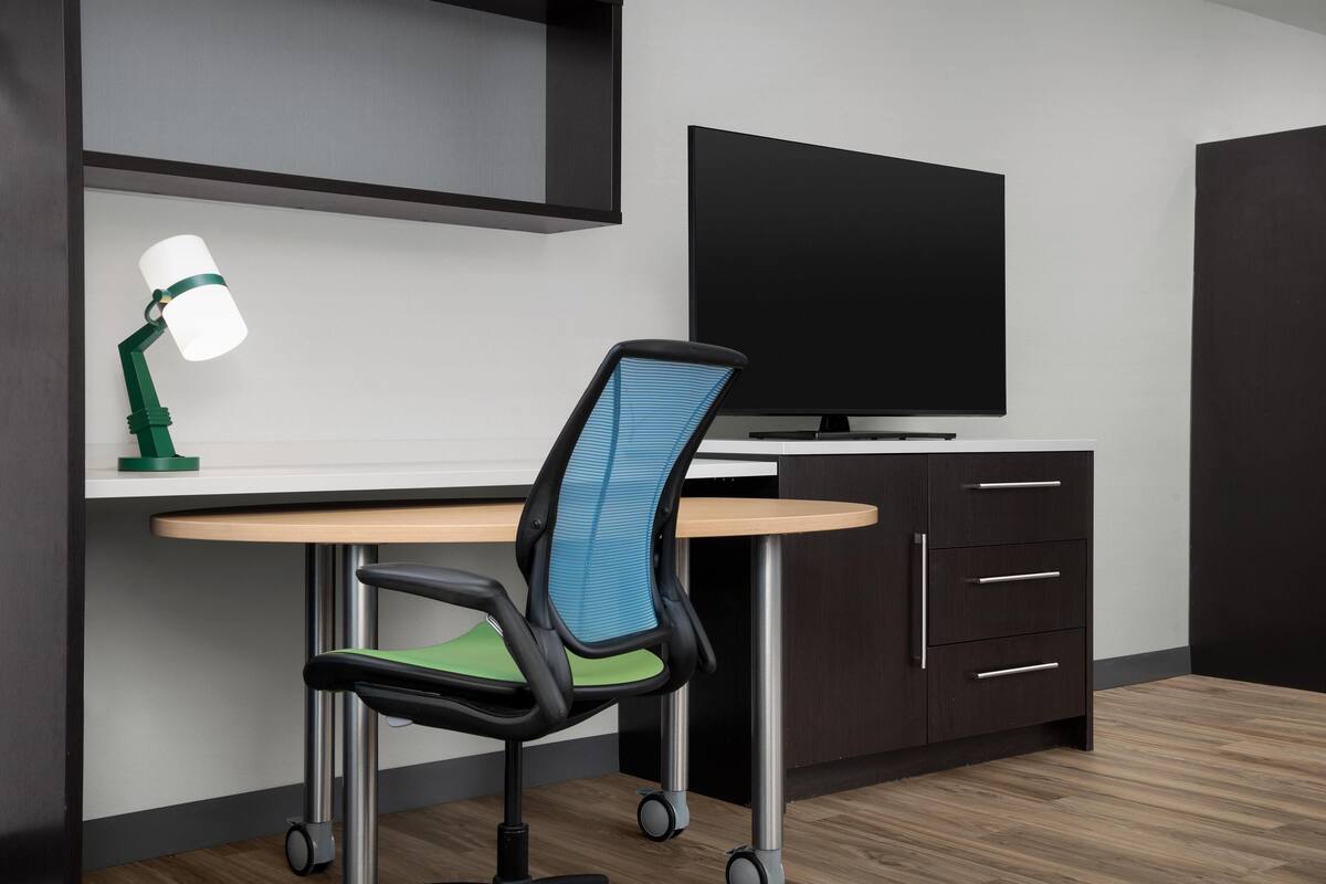 Ein moderner Arbeitsplatz mit Schreibtisch, Stuhl, Fernseher und Schränken.