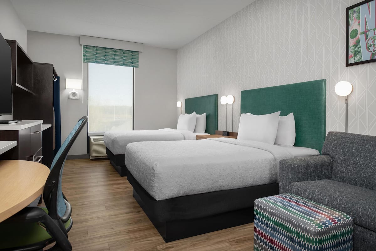 Ein Hotelzimmer mit zwei Betten, einem Schreibtisch, einem Sessel und einem kleinen Hocker.