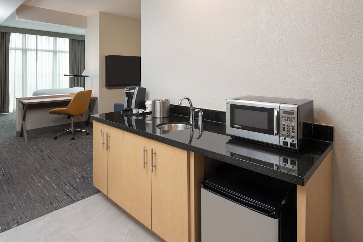 A modern hotel room with a kitchenette, a bed, a desk, and a chair.
