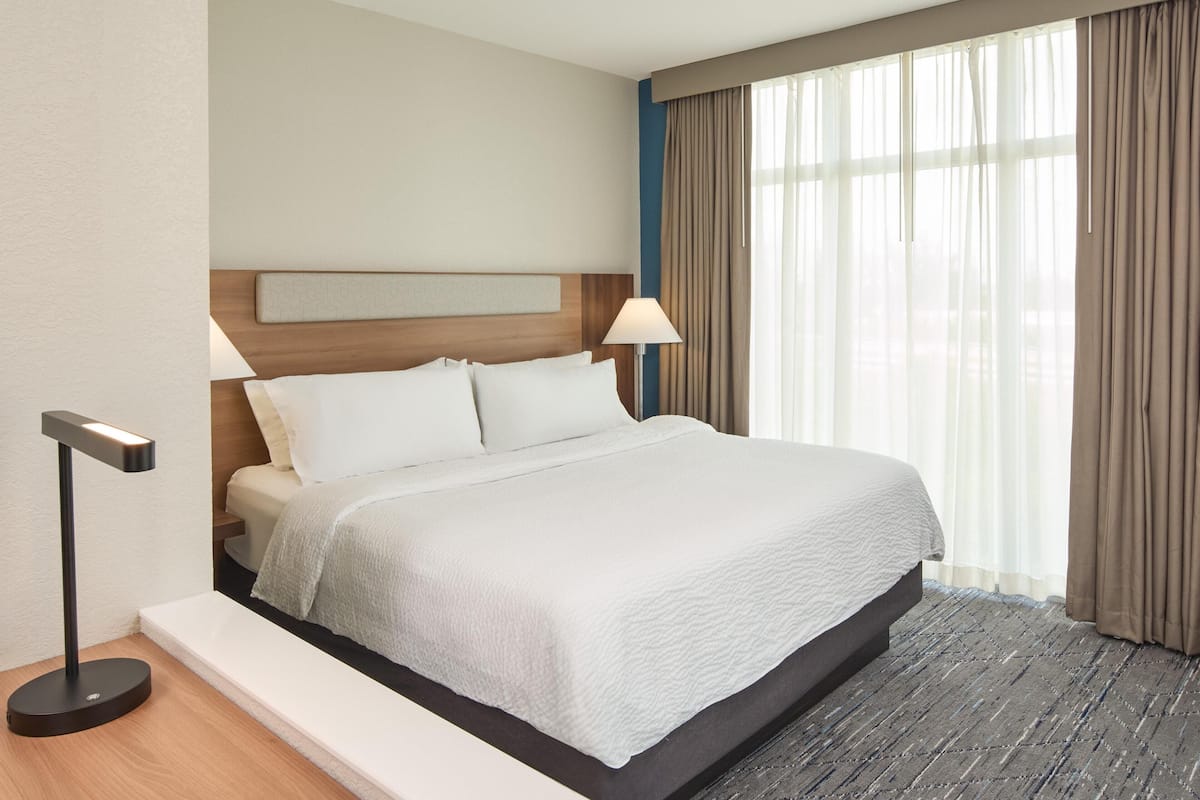 A hotel room with a bed, a bedside lamp, a headboard, and a window with curtains.