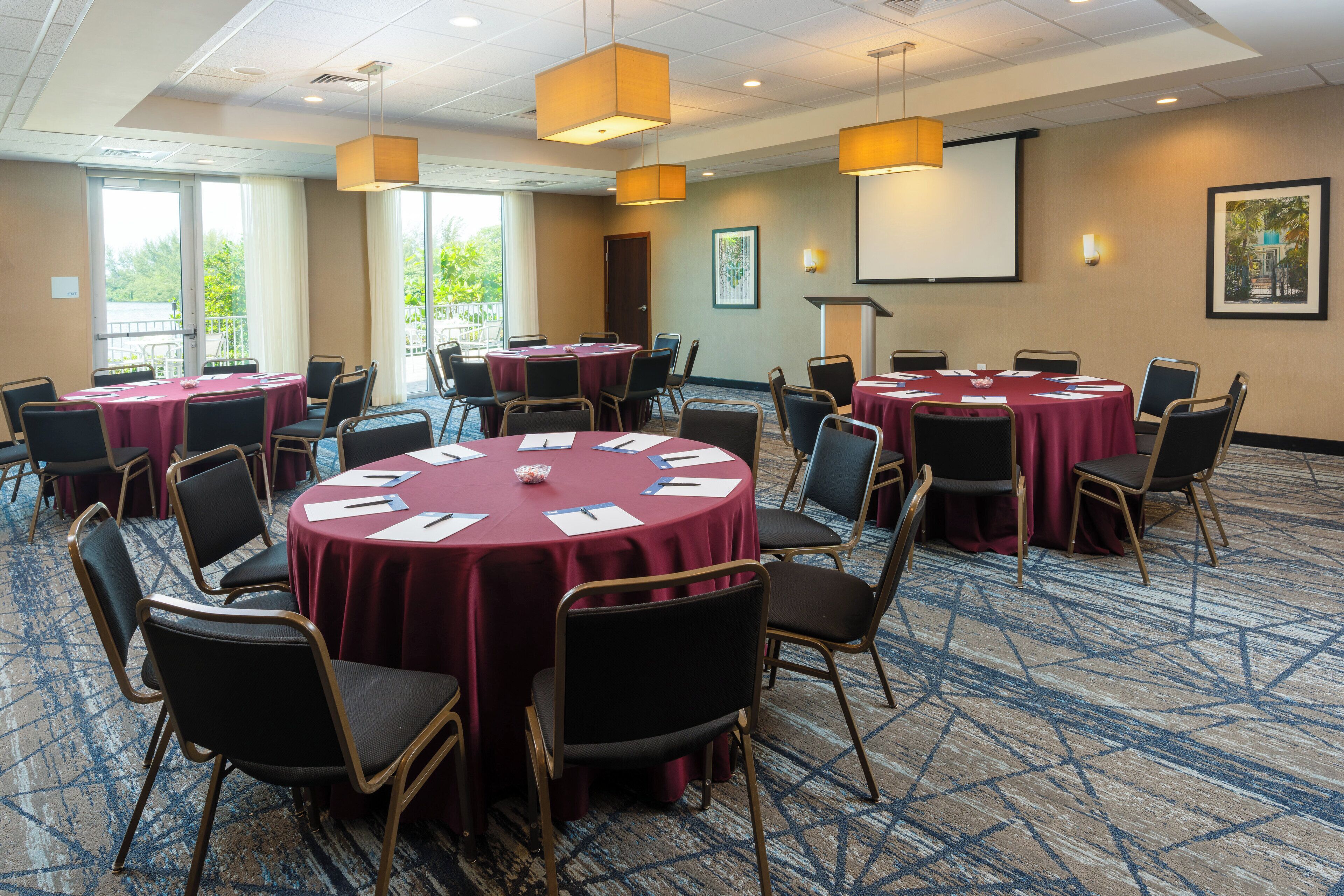 A conference room with round tables, chairs, and a projector screen.