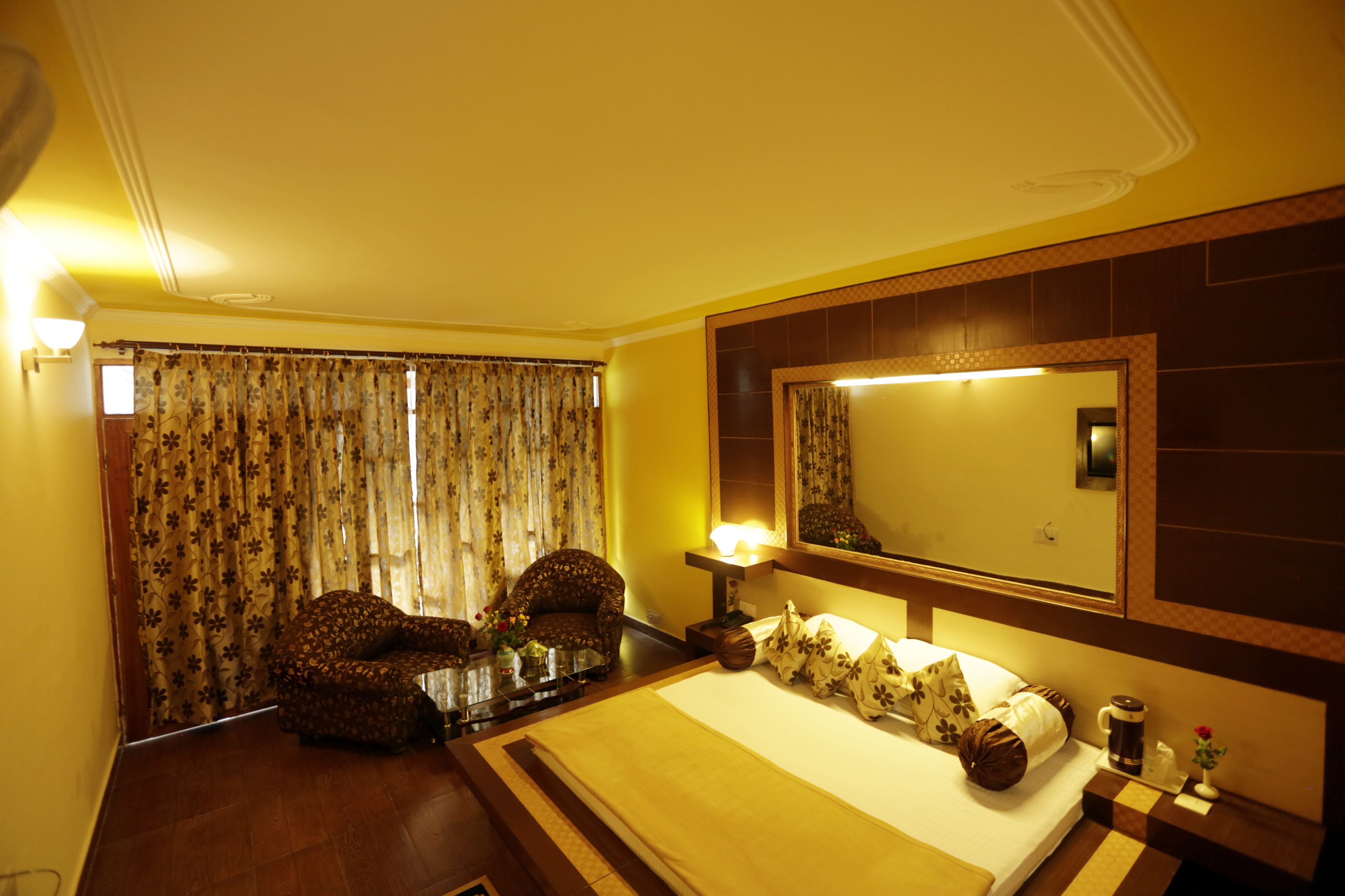 A hotel room with a large bed, a chair, a desk with a lamp, a mirror, and curtains.