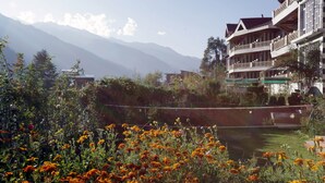 Un hotel con vistas a montañas, un jardín con flores y un balcón con barandilla.