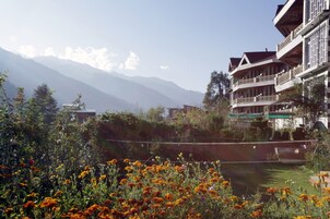 A hotel with a view of mountains, a garden with flowers, and a balcony with a railing.