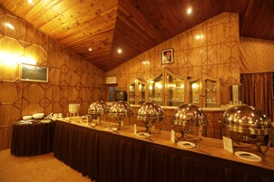 A buffet setup with multiple food service stations, wooden paneling on the walls, and a ceiling with wooden beams.