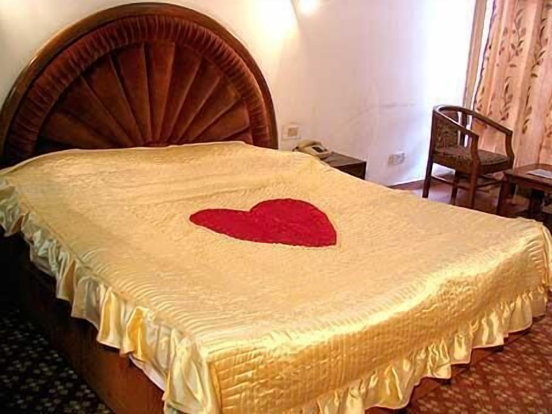 Una cama con un cojín con forma de corazón, un cabecero de madera y una mesita de noche con una lámpara.