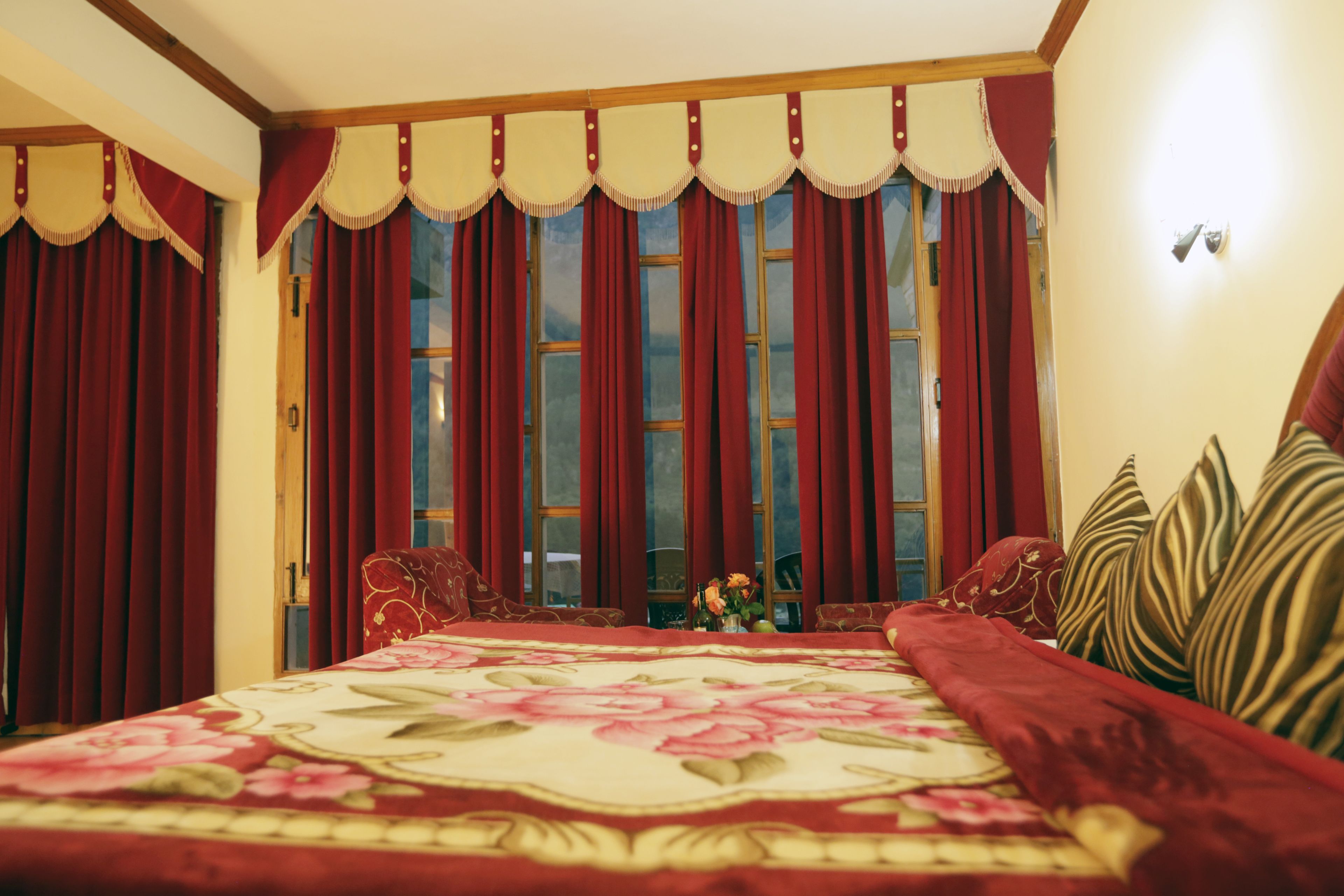 A bedroom with a large bed, red curtains, and a floral bedspread.