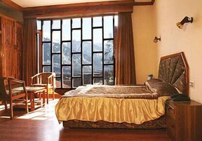 A bedroom with a large window, wooden furniture, and a bed with a patterned bedspread.