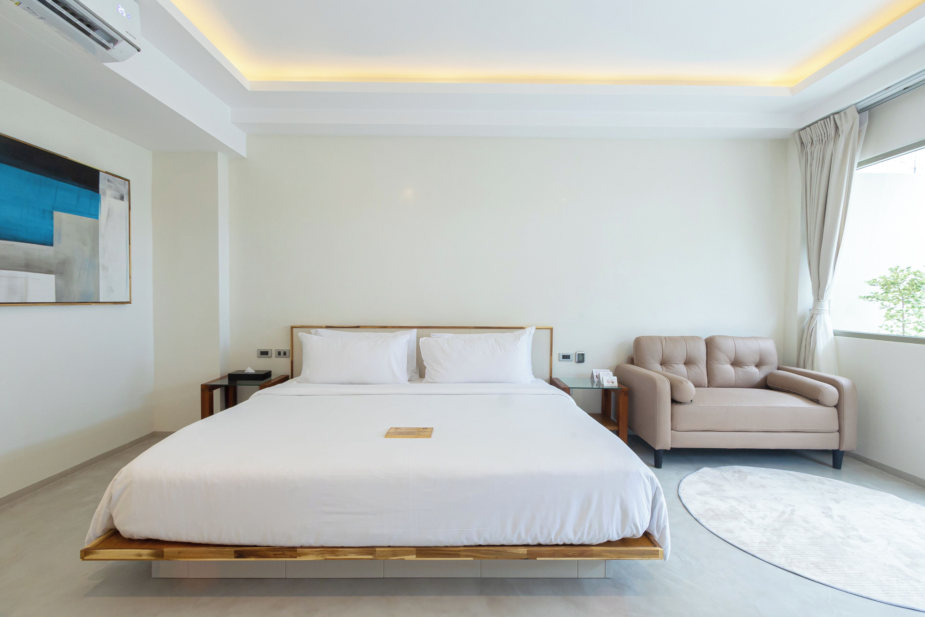 A modern hotel room with a large bed, a sofa, and a view of the outdoors.