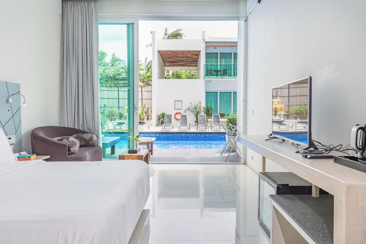 A hotel room with a bed, a desk with a computer, a TV, and a view of an outdoor swimming pool.