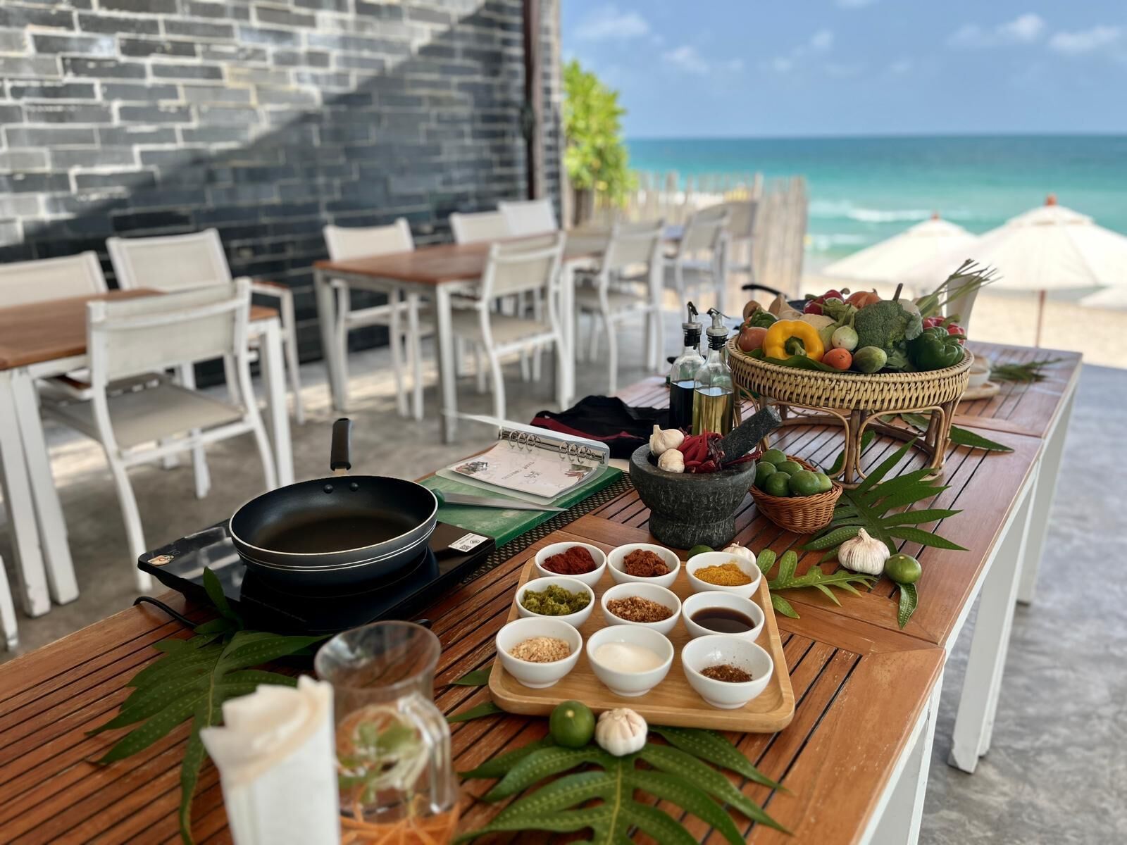 A wooden table with a variety of condiments, a mortar and pestle, and fresh vegetables.