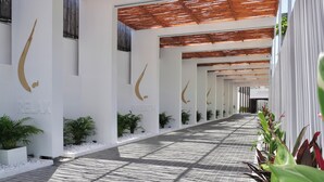 A corridor with white walls, a tiled floor, and a series of potted plants. - KC Beach Hotel Samui (Koh Samui)