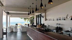 A modern bar area with a view of the ocean, white wicker furniture, and a variety of bar tools and bottles. - KC Beach Hotel Samui (Koh Samui)