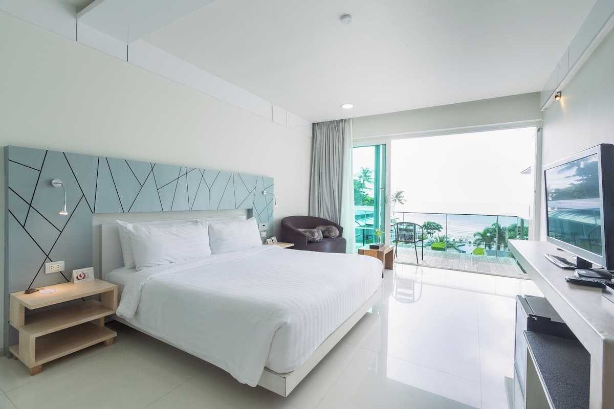 A modern hotel room with a large bed, a TV, and a balcony with a view of the outdoors.