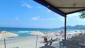 A beachside restaurant with outdoor seating, umbrellas, and a view of the ocean. - KC Beach Hotel Samui (Koh Samui)