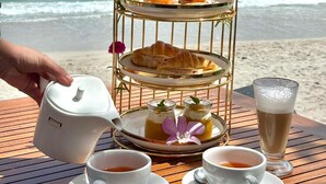 A seaside table with a tiered serving tray, two cups of tea, a glass of iced coffee, and a teapot. - KC Beach Hotel Samui (Koh Samui)