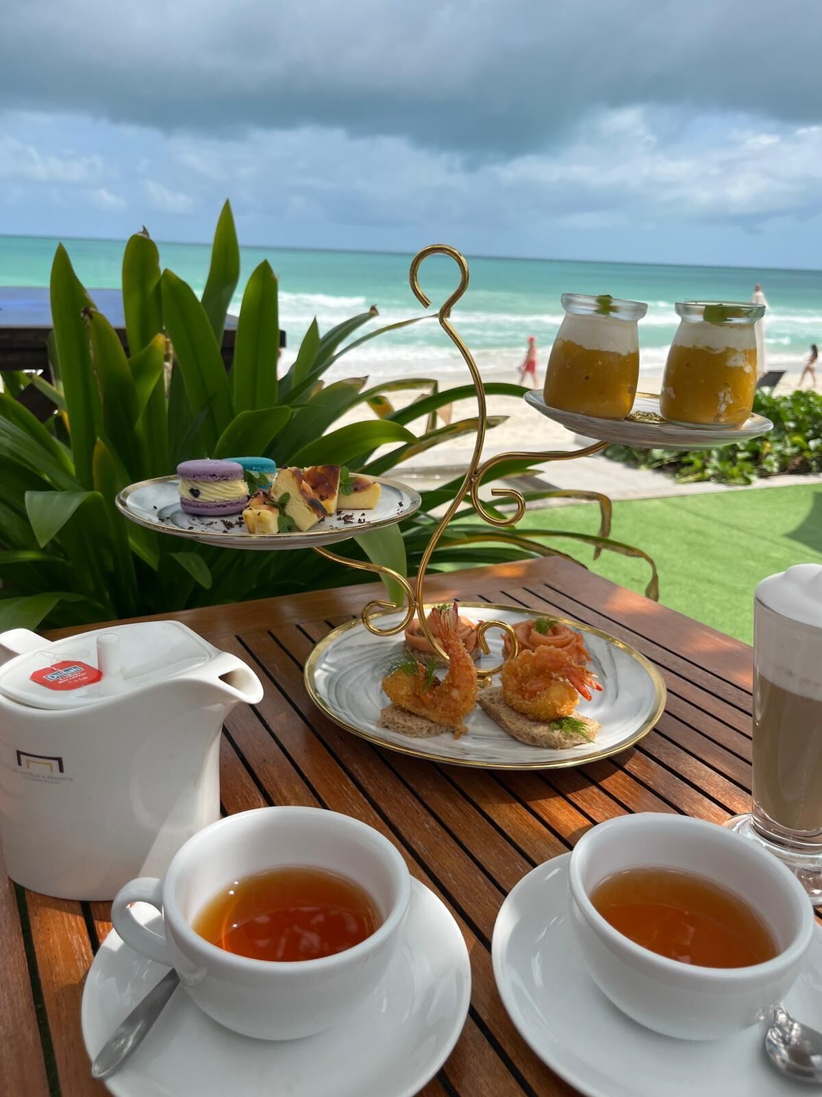 A table with food and drinks, a teapot, and a view of the beach.