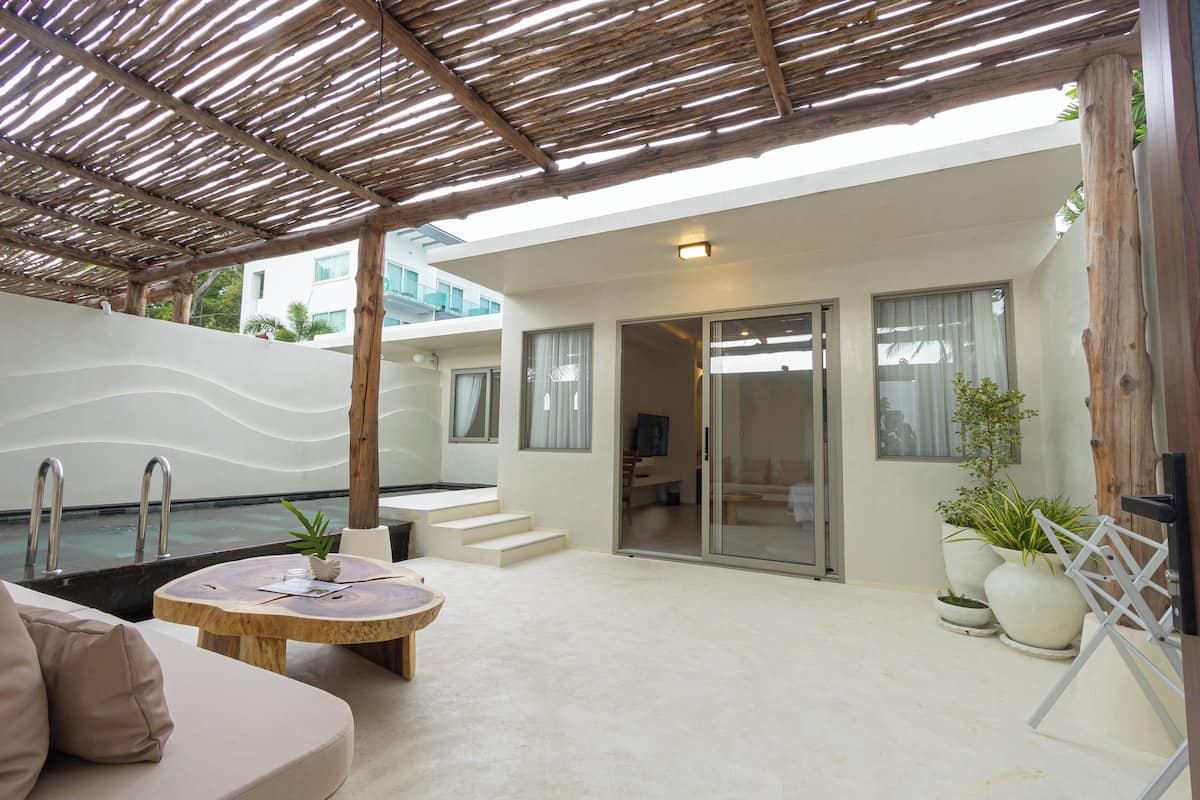 A modern outdoor living area with a pool, a wooden pergola, and a seating area with a sofa and a round table.