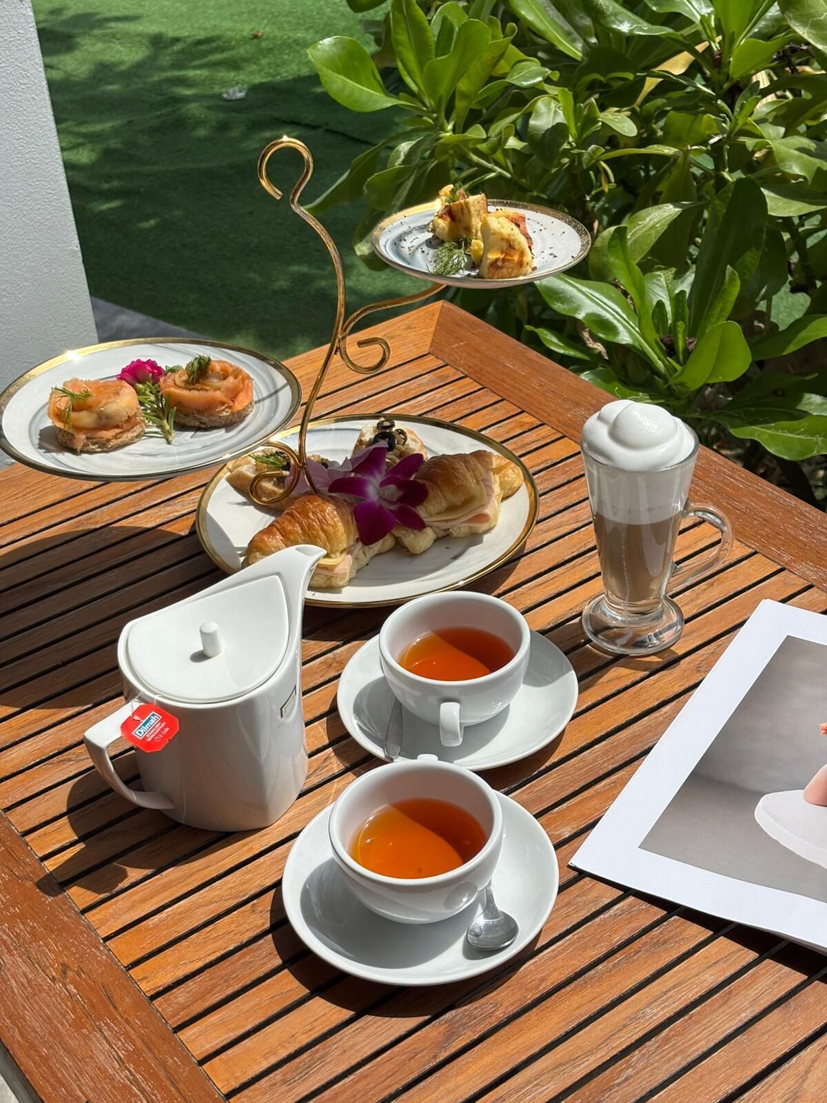 Una mesa con un calentador de agua, dos tazas de té, un vaso de café helado y platos de comida.
