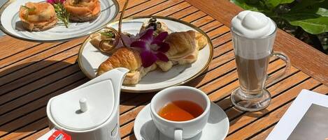Una mesa con un calentador de agua, dos tazas de té, un vaso de café helado y platos de comida.