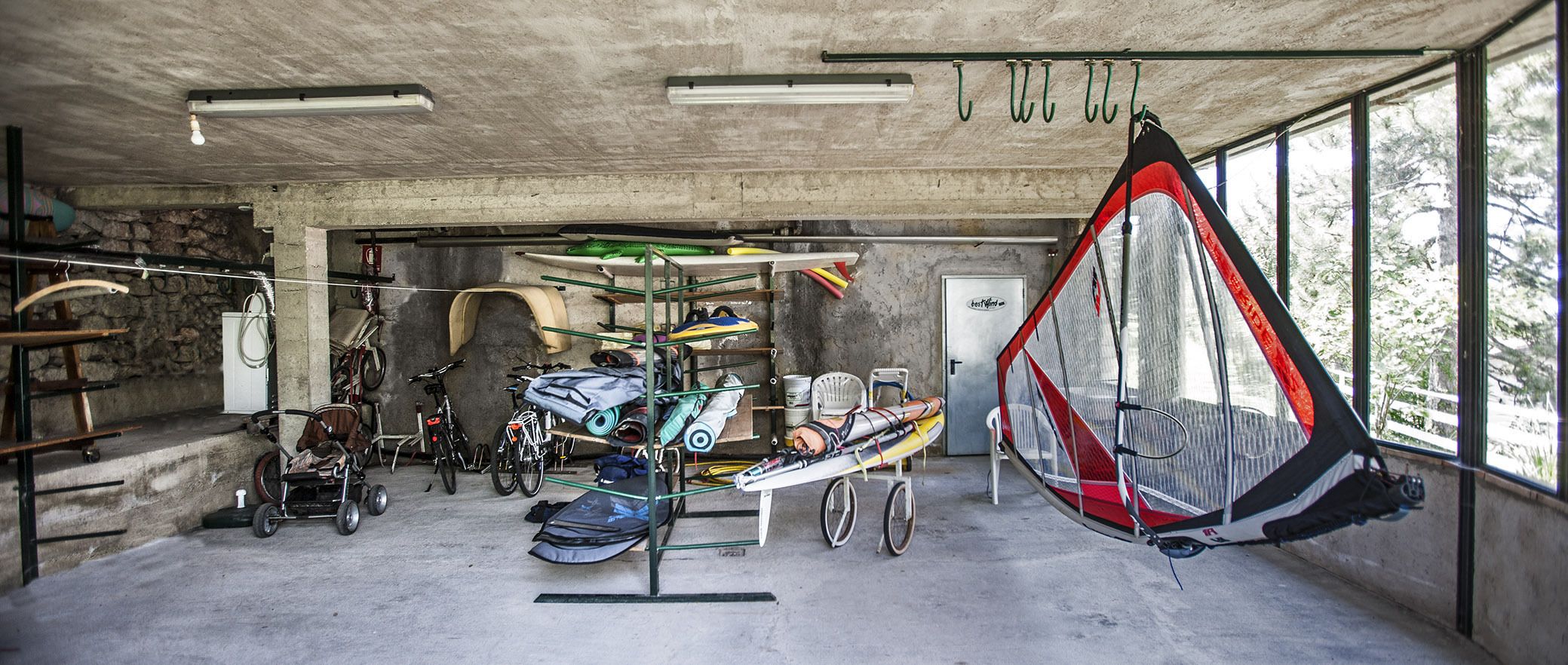 Une pièce spacieuse avec un plafond en béton, de grandes fenêtres et divers équipements de plein air, comme des kayaks et des vélos.