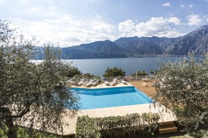 Una piscina con sillones de descanso, rodeada de árboles, con vistas a un lago y montañas.