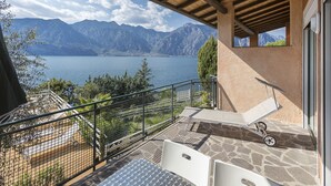 Un balcón con vistas a un lago y montañas, una mesa y una silla.
