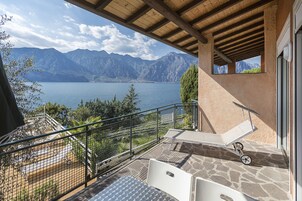Un balcón con vistas a un lago y montañas, una mesa y una silla.