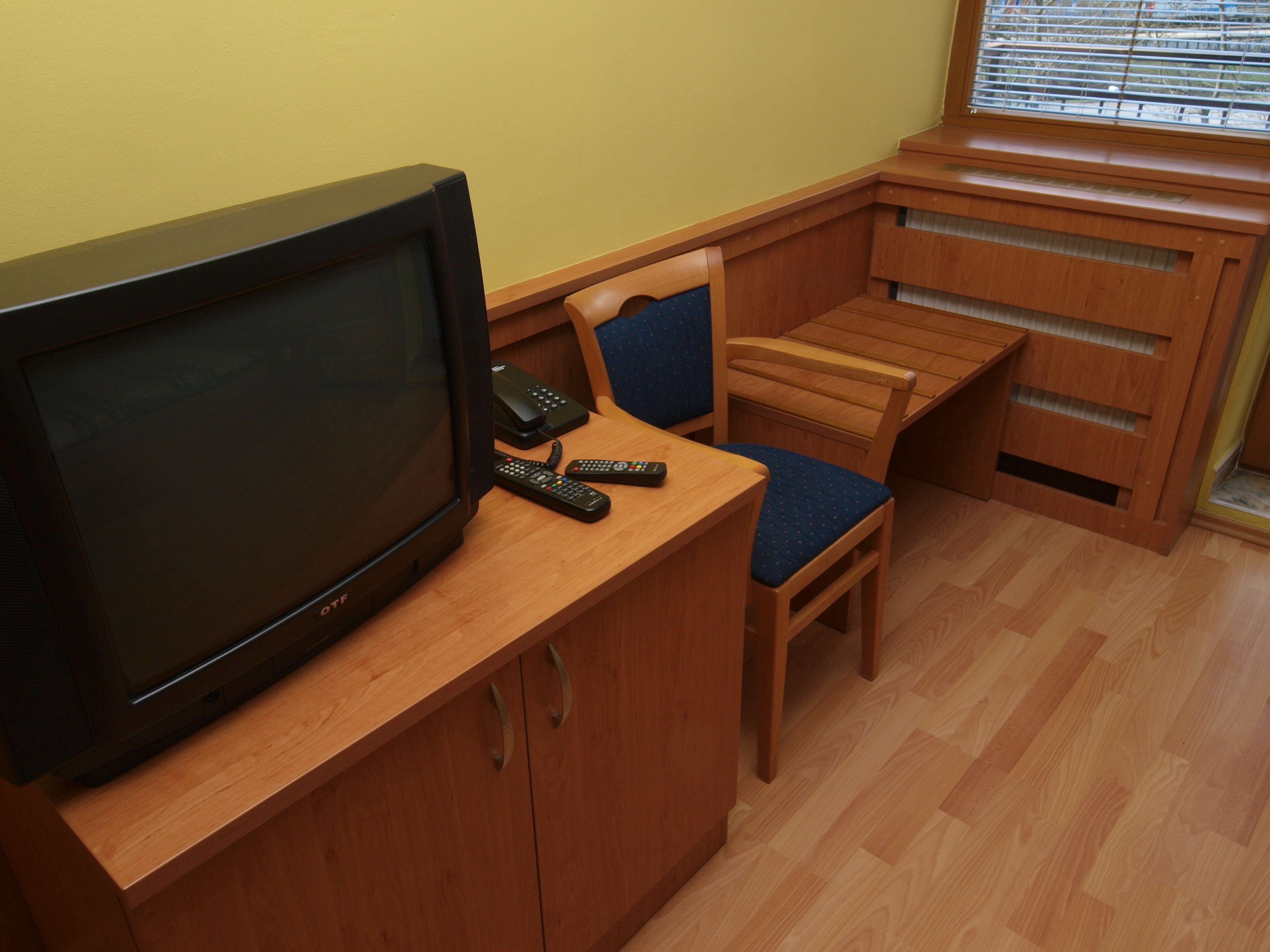 A compact living space with a television, a small table, a chair, and a window with blinds.