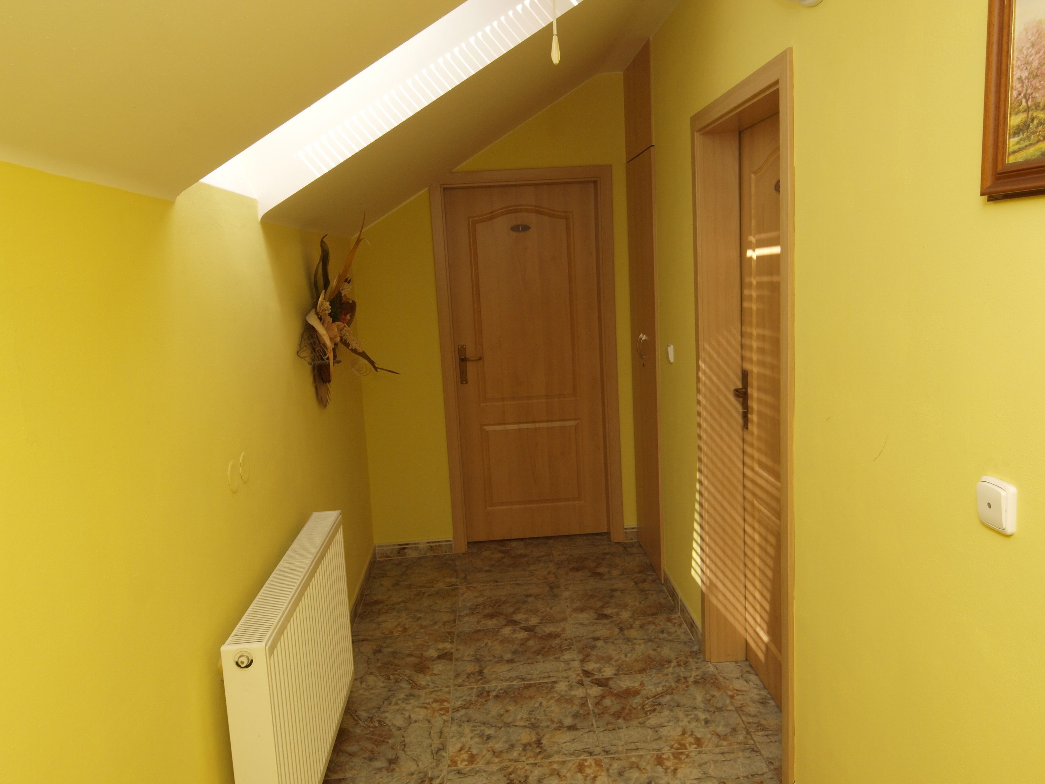 A narrow hallway with yellow walls, a wooden door at the end, and a radiator on the left.