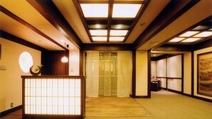 A traditional Japanese interior with tatami flooring, shoji screens, and a reception area with a lit screen. - Kamogawa-kan Inn (Kyoto)