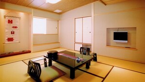 A traditional Japanese-style room with tatami flooring, a low table, and a television mounted on the wall. - Kamogawa-kan Inn (Kyoto)