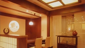 A dining area with a wooden table and chairs, a wall-mounted clock, and a decorative vase on a console table. - Kamogawa-kan Inn (Kyoto)
