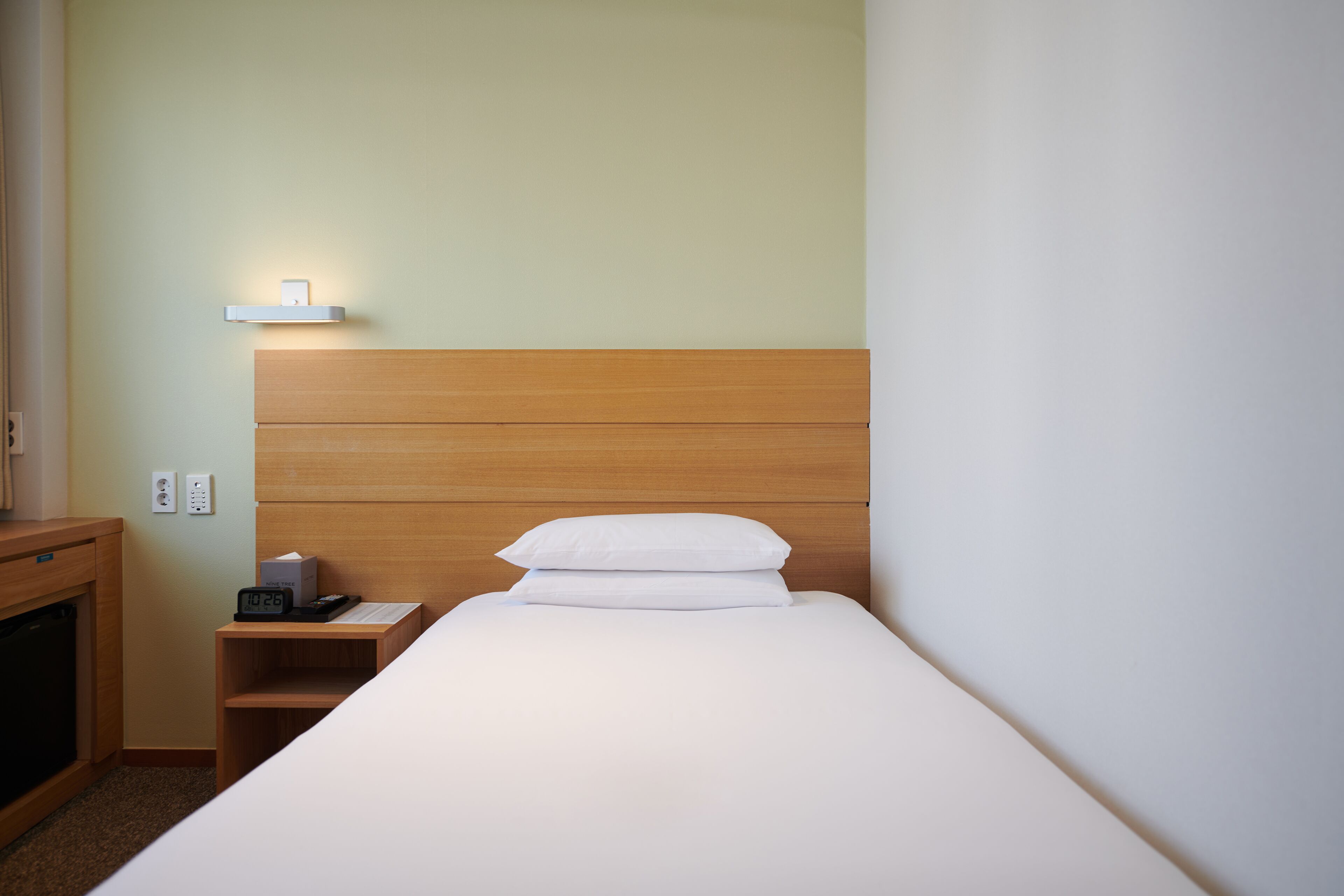 A neatly made bed with white bedding, a wooden headboard, and a bedside table with a clock and a box.