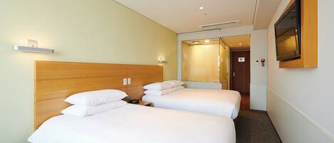 Habitación de hotel con dos camas, cabecera de madera, televisor de pantalla plana montado en la pared y un estante pequeño con luz.