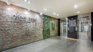A modern interior with a brick wall, a glass elevator, and a tiled floor. - NINE TREE BY PARNAS SEOUL MYEONDONG 1 (Seoul)