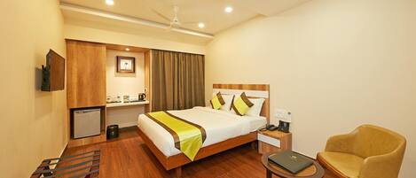 A hotel room with a bed, bedside table, chair, desk, and a small kitchenette.