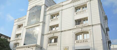 Un edificio de varios pisos con un estilo arquitectónico clásico, que cuenta con ventanas amplias y balcones. El edificio tiene un letrero destacado para 'Taj Kamar Inn'.