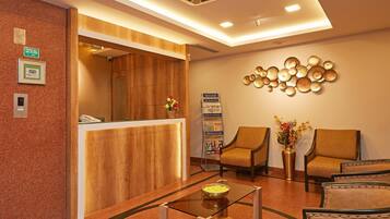 Zona de recepción de hotel con un mostrador de madera, dos sillones, una mesita de centro y un adorno en la pared.