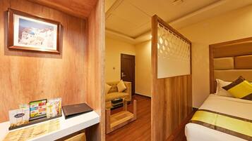 Habitación de hotel con un escritorio de madera, una cama con almohadas amarillas, un sofá y un separador de madera.