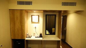 Habitación de hotel compacta con una pared de acento de madera, un escritorio pequeño con una lámpara, un cuadro enmarcado y una ventana con cortinas.