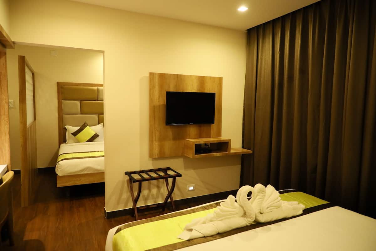 Habitación de hotel con cama, televisor montado en un panel de madera, estante pequeño, perchero y cortina.