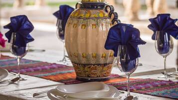 Una mesa dispuesta con una jarra de cerámica decorativa, copas de vino y un mantel individual colorido.