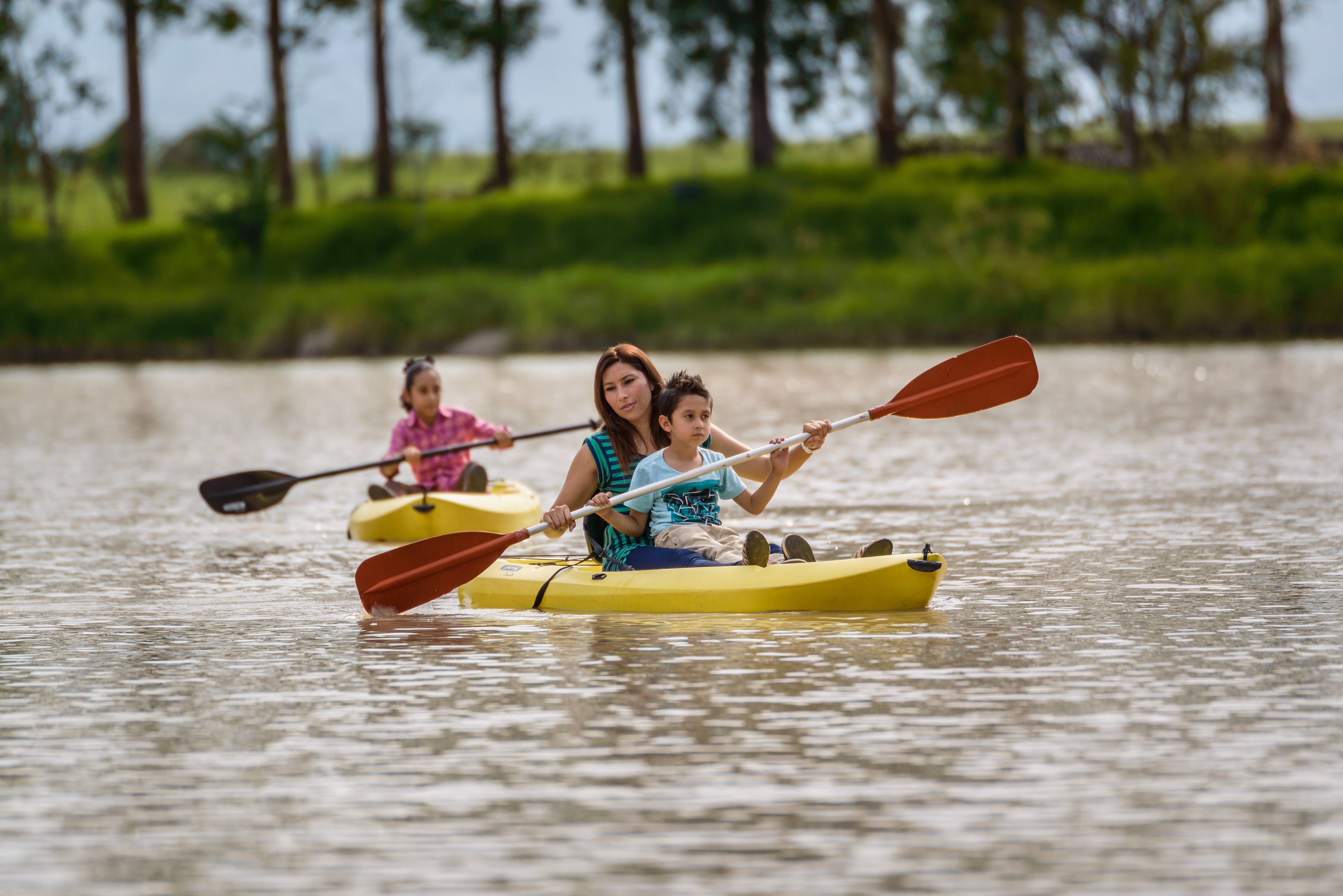 Un groupe de personnes se trouve dans un kayak jaune sur une étendue d’eau calme, avec une rive verdoyante en arrière-plan.