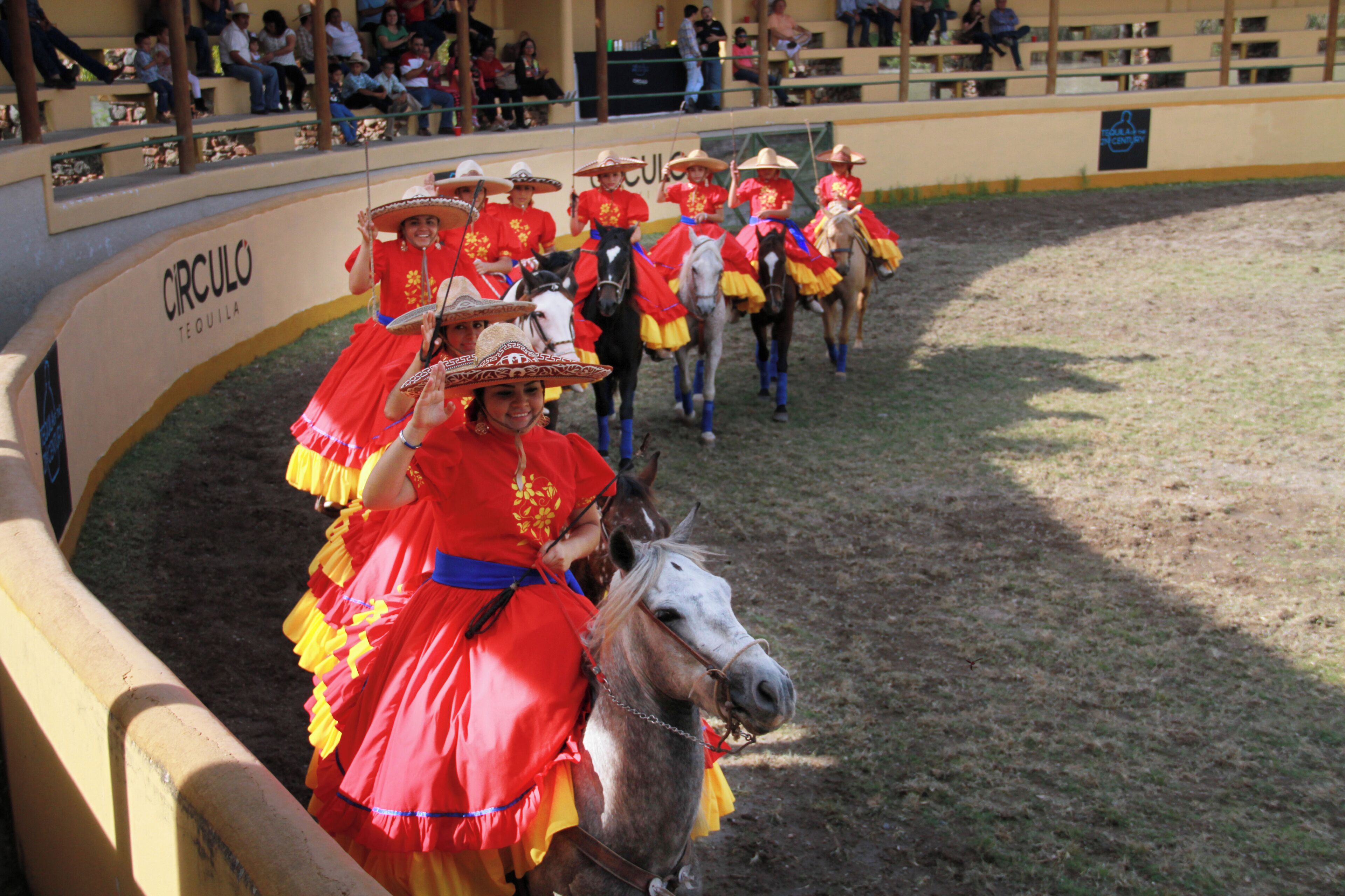 A group of people in traditional attire riding horses in an arena.
