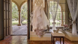 Un vestido de novia exhibido en una habitación con vistas a un jardín, a través de una puerta abierta.