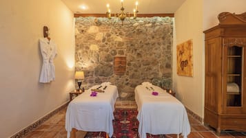 Relax in a serene spa room with two massage tables, a stone wall backdrop, and a comfortable robe.