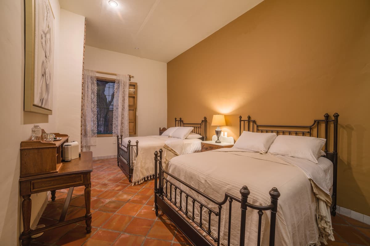 Un dormitorio con dos camas, una mesita de noche, una mesa y una ventana con cortinas.