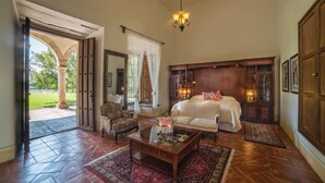 Amplia habitación con una cama grande, una zona de estar con una mesita de café y vistas a un espacio exterior con una columna y vegetación.