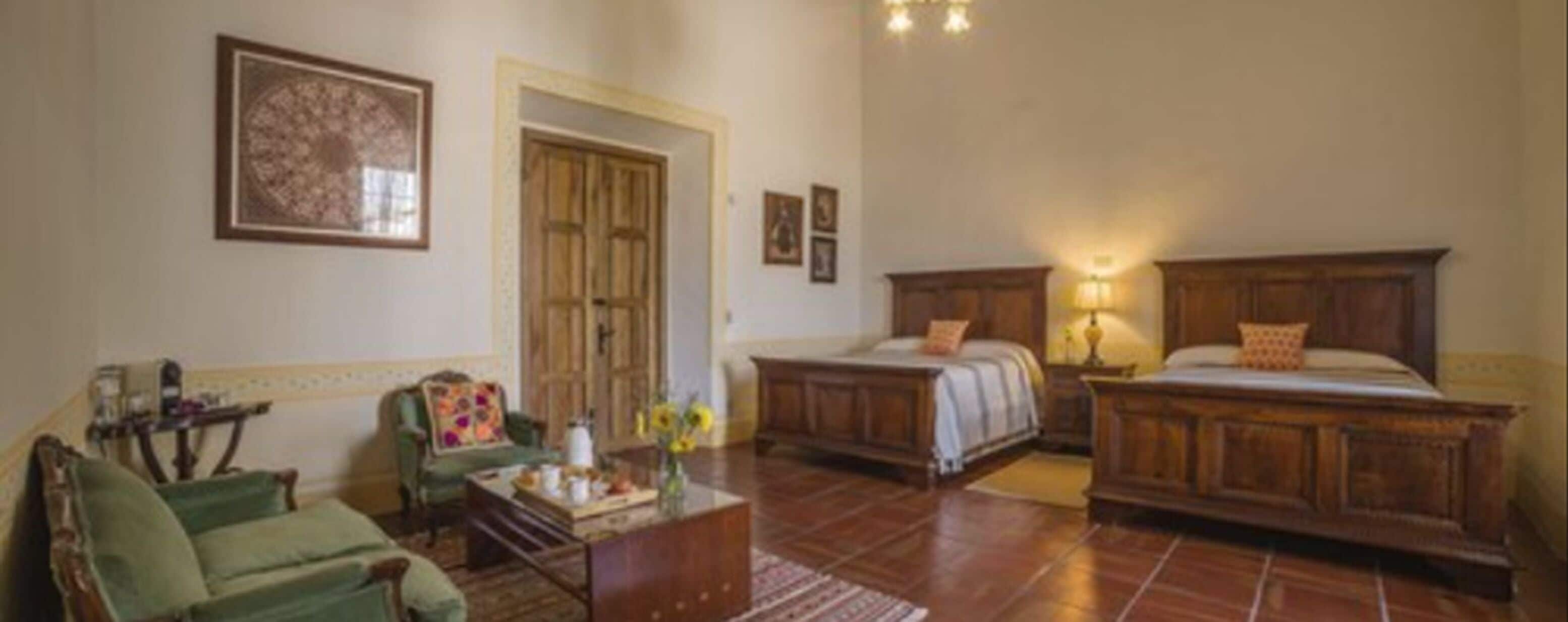 A room with a bed, a green armchair, a wooden dresser, and a painting on the wall.